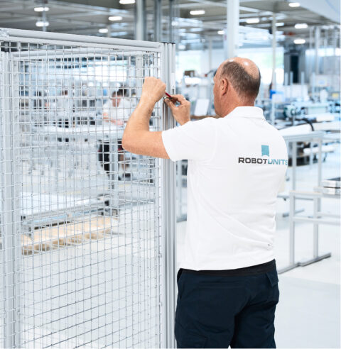 Ein Robotunits-Mitarbeiter von hinten im weißen Poloshirt montiert Schutzzäune.